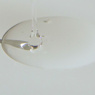 Image of MCT oil being poured and dropped on a white surface. The liquid is clear.