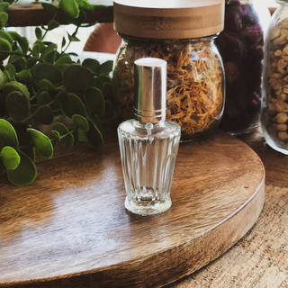 Perfume bottle sits on a timber surface with dried calendula in the back ground