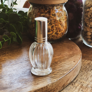 Empty round shaped perfume bottle sits on a timber surface in front of dried flowers