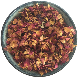 Ceramic bowl filled with red rose petals that are dried. Image has a white background