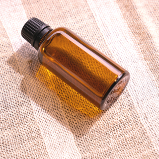 A 50ml amber glass bottle lays on a hessian surface