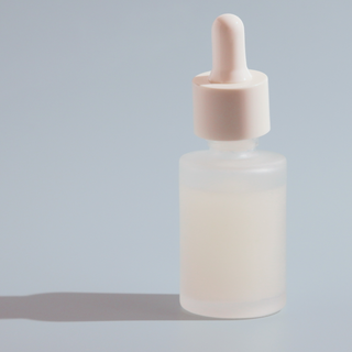 A white frosted clear dropper bottle sits on a pale blue surface. The dropper bottle is for purchase in Australia