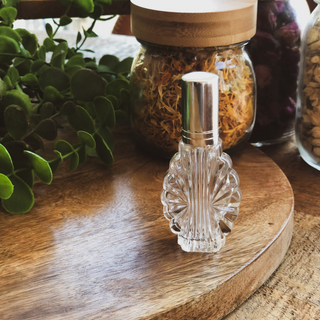 Vintage style perfume bottle sits on a timber surface in front of dried flowers