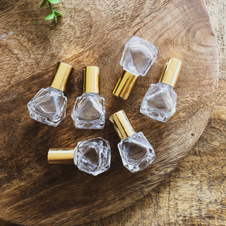 A group of 6 glass roller bottles with gold lids lay on their side on a wooden surface