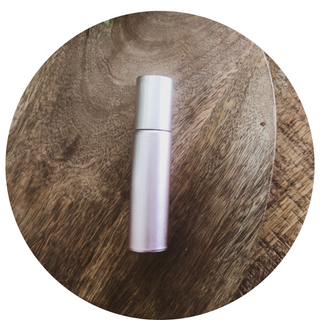 a pink 10ml roller bottle lays on a timber surface