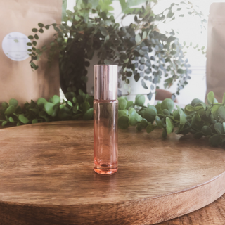 translucent pink roller bottle stands on a timber surface with plants in the background