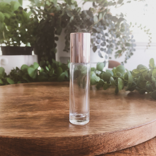 rose gold cap and clear roller bottle that holds 10ml sits on a timber bench with green plants in the background